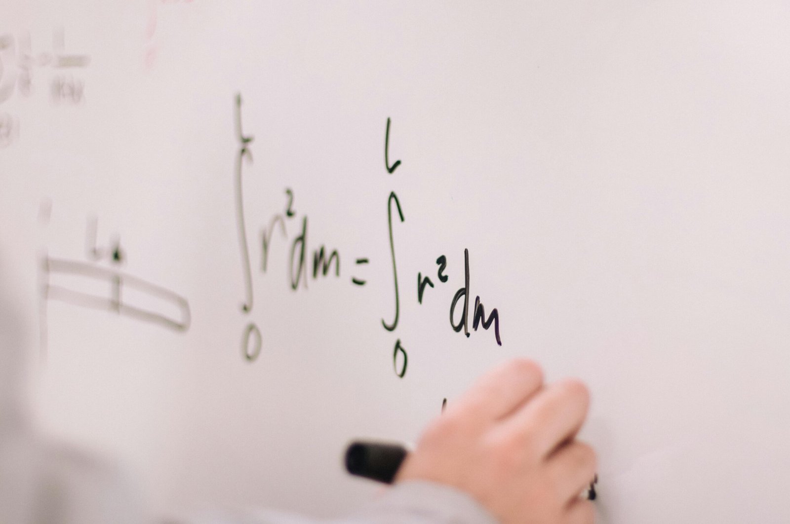 Person writing math equations on a whiteboard, focusing on integrals and formulas.
